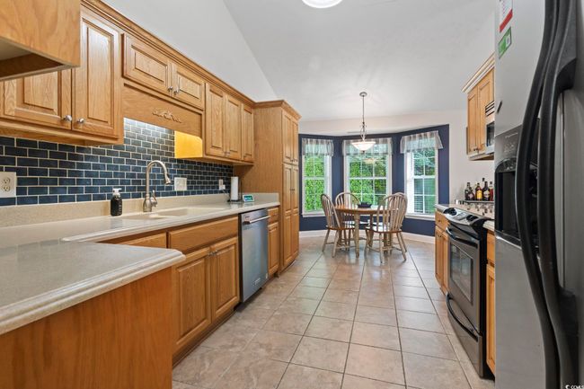 Kitchen featuring stainless steel appliances, light tile patterned floors, light countertops, decorative backsplash, and decorative light fixtures | Image 15