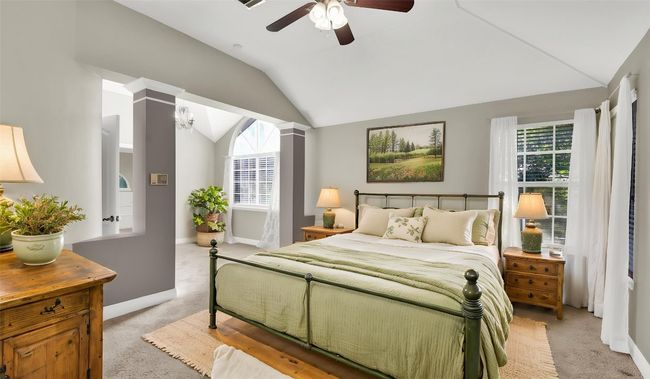 Primary bedroom featuring light colored carpet, vaulted ceiling, decorative columns, baseboards, and ceiling fan (virtually staged) | Image 12