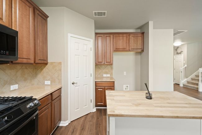 Kitchen with wooden counters, dark wood-style flooring, a kitchen island, and black gas range | Image 16