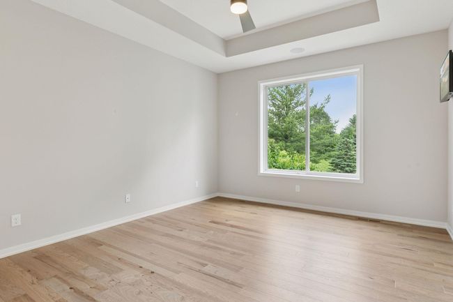 Primary bedroom offers custom features of box trayed ceiling, ceiling fan with light and hardwood floors | Image 25
