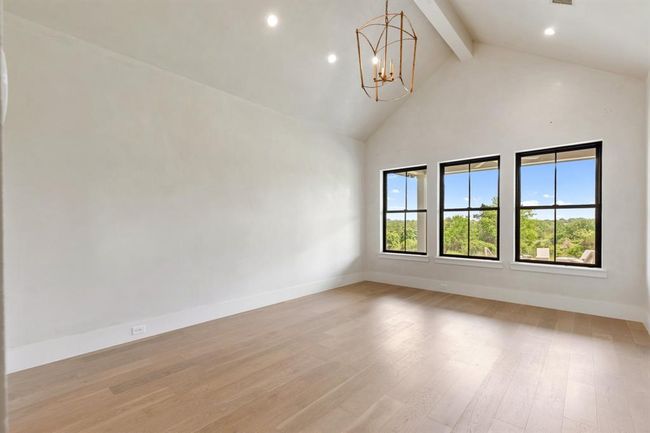 The primary suite features triple oversized windows with a view to the rear pasture. Segreto installed a neutral plaster treatment on all walls which offer a subtle sheen. The wood beam accentuates the vaulted ceiling. The primary suite is located away from other bedrooms to offer privacy. The engineered hardwood floors extend throughout this space as well. | Image 17