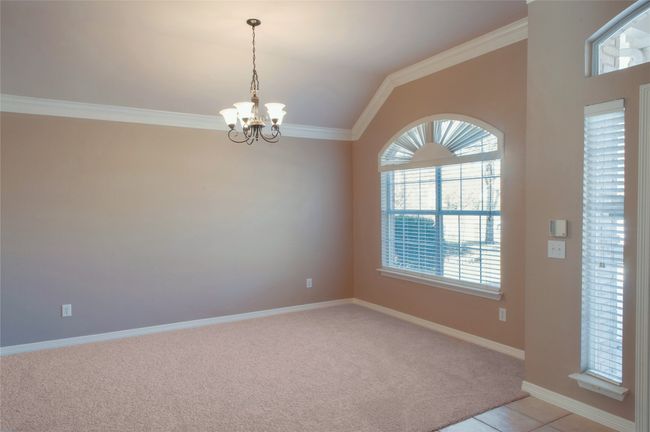 Spare room featuring a chandelier, light colored carpet, crown molding, lofted ceiling, and baseboards | Image 9