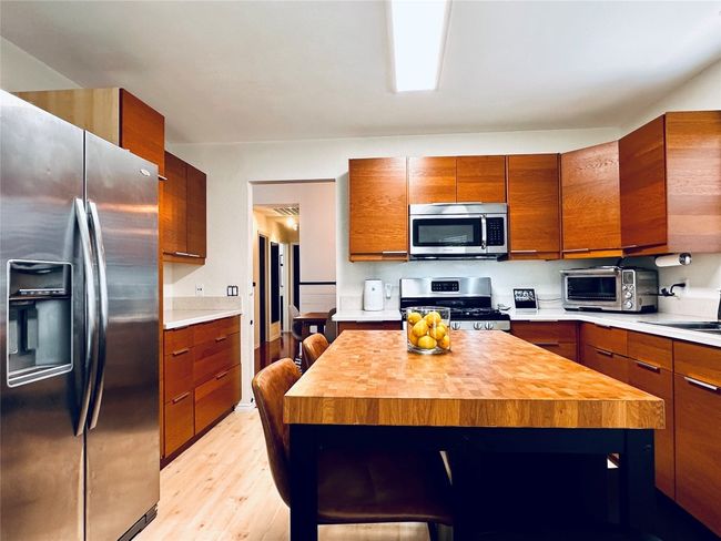 Kitchen with light wood-type flooring, wood counters, a center island, brown cabinetry, and stainless steel appliances | Image 9