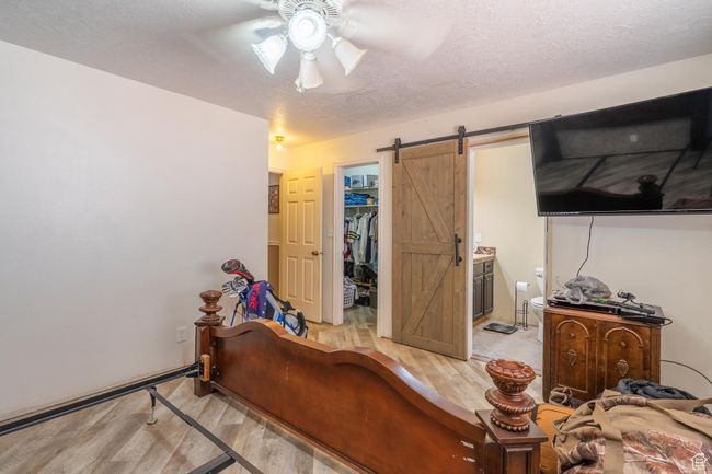Bedroom with light wood-style flooring, a barn door, a walk in closet, a closet, and a textured ceiling | Image 34