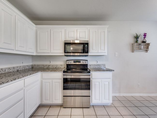 Kitchen featuring appliances with stainless steel finishes, white cabinetry, light tile patterned floors, and light stone counters | Image 14