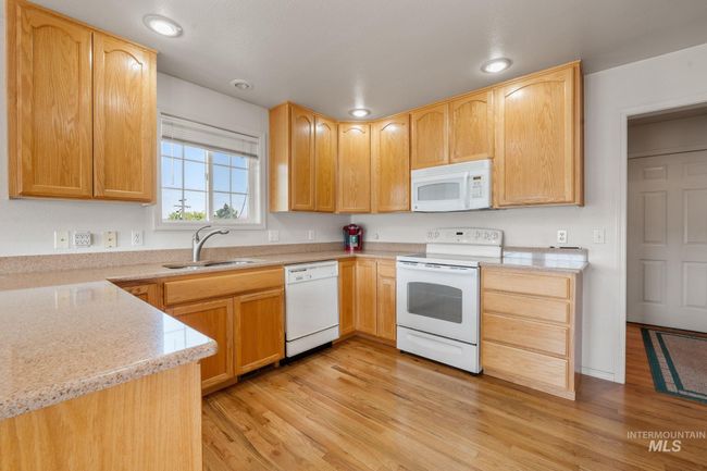 Kitchen featuring white appliances, light wood-style flooring, light countertops, light brown cabinetry, and recessed lighting | Image 10