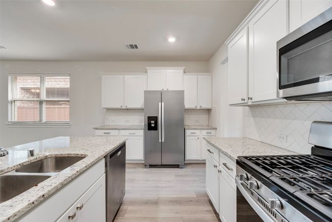 Kitchen featuring appliances with stainless steel finishes, light wood-type flooring, white cabinetry, decorative backsplash, and recessed lighting | Image 21
