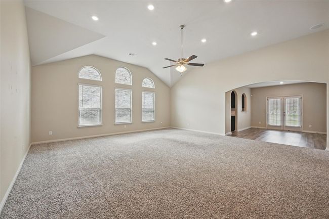 Unfurnished living room with ceiling fan, arched walkways, vaulted ceiling, carpet floors, and baseboards | Image 5