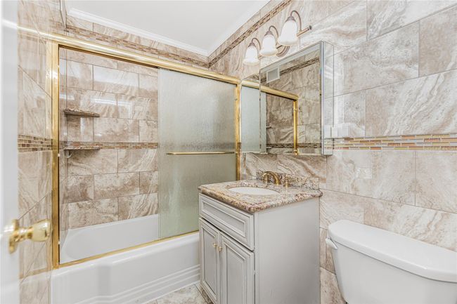 Full bathroom with crown molding, vanity, bath / shower combo with glass door, and tile walls | Image 9