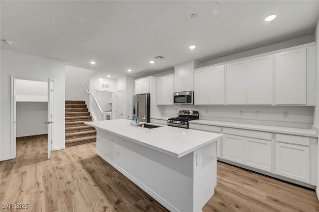 Kitchen with stainless steel appliances, light countertops, white cabinets, a sink, and a center island with sink | Image 16