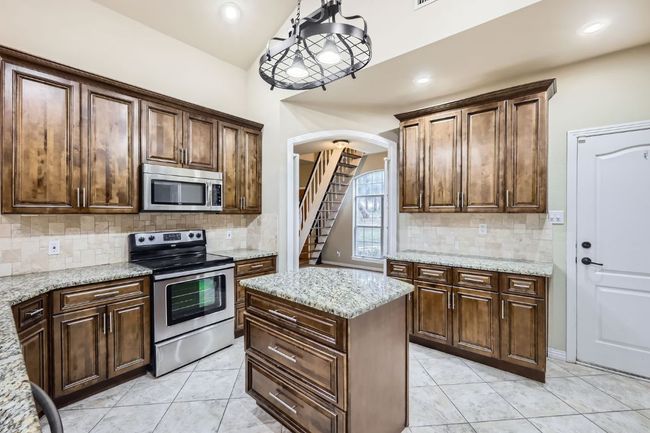 Kitchen with appliances with stainless steel finishes, arched walkways, backsplash, light tile patterned flooring, and light stone counters | Image 7