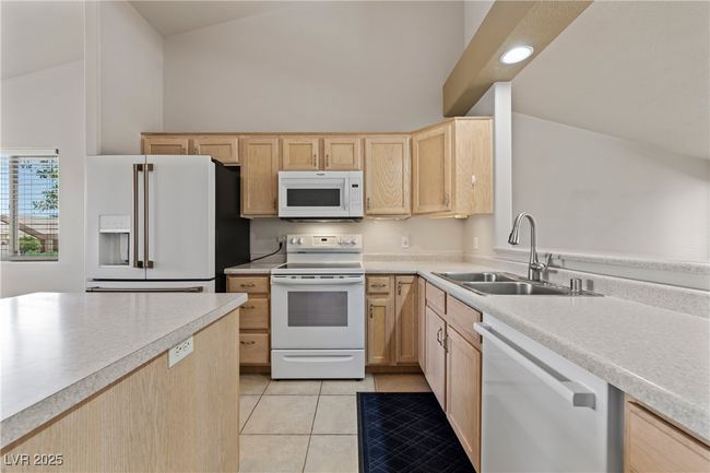 Kitchen with white appliances, light brown cabinets, high vaulted ceiling, light countertops, and light tile patterned floors | Image 20