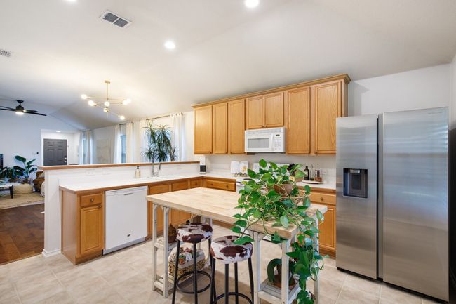 Kitchen with white appliances, a peninsula, lofted ceiling, a ceiling fan, and a chandelier | Image 11