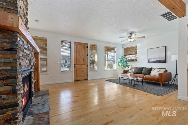 Living room featuring light wood-style floors, a textured ceiling, ceiling fan, and a stone fireplace | Image 12