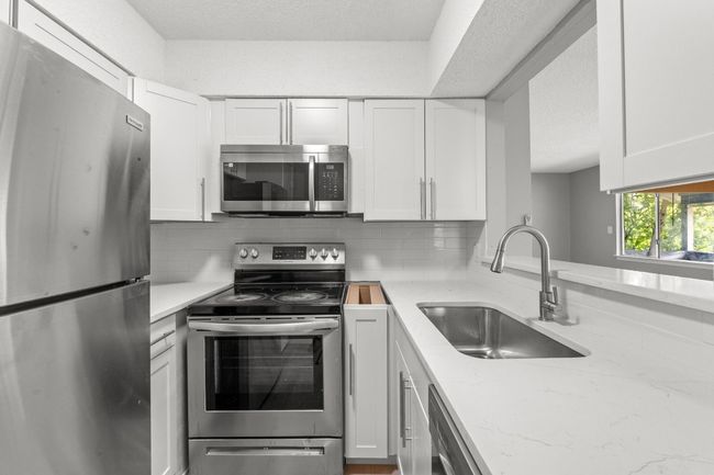 Kitchen with stainless steel appliances, a sink, backsplash, white cabinetry, and light stone countertops | Image 11