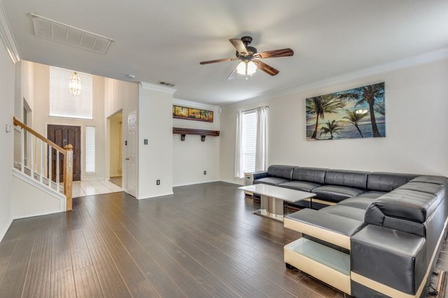 Living room with crown molding, stairway, visible vents, ceiling fan, and wood finished floors | Image 8