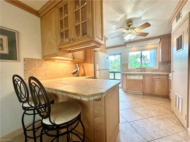 Kitchen featuring a breakfast bar, freestanding refrigerator, dishwasher, backsplash, and a ceiling fan | Image 9