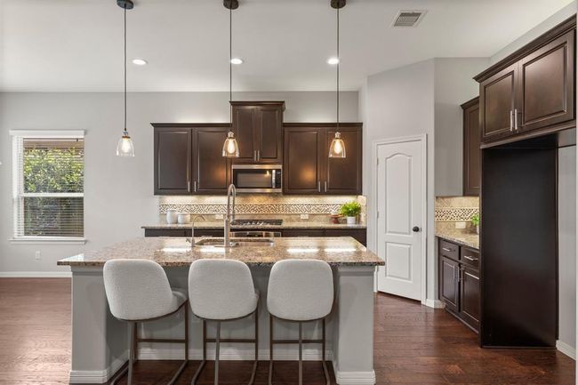Stunning kitchen with rich espresso cabinetry, granite counters, custom backsplash, under and over cabinet lighting and a spacious island with counter depth seating | Image 13