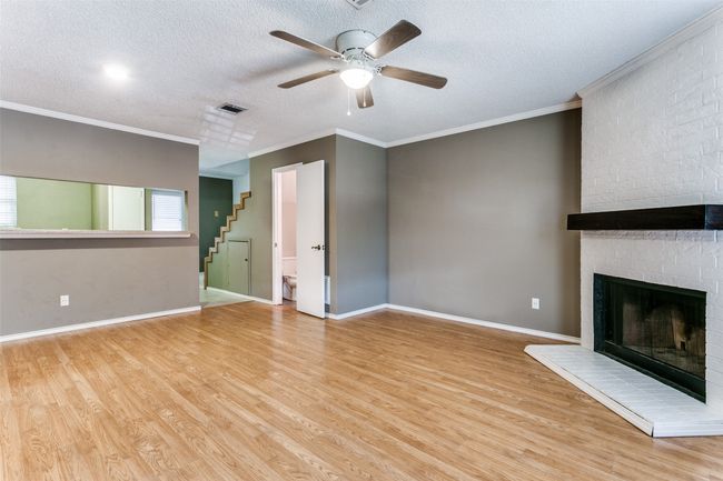 Unfurnished living room featuring wood finished floors, a ceiling fan, a fireplace, a textured ceiling, and stairway | Image 6