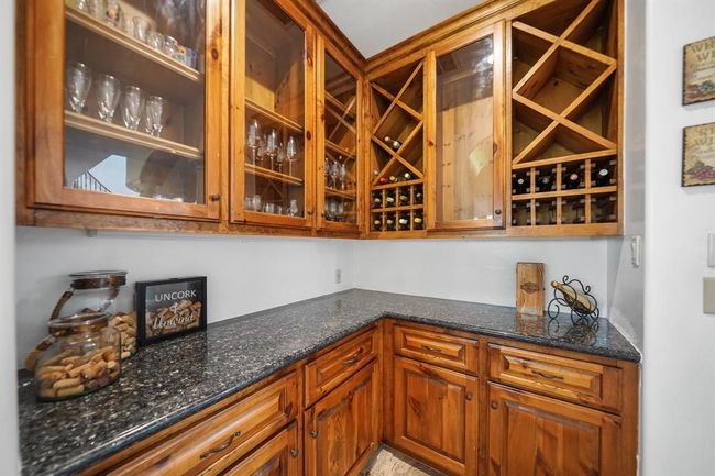 Conveniently located between the kitchen and formal dining area is a butler's pantry with wood-stained custom cabinets with glass display fronts, built-in wine storage racks, a granite surfaced serving bar with additional cabinet and drawer storage below & tile flooring. | Image 12