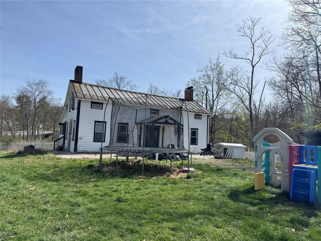Back of house featuring a standing seam roof, a chimney, a storage shed, and a trampoline | Image 33
