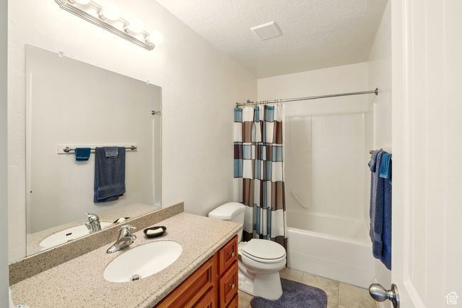 Bathroom with vanity, tile patterned floors, shower / bath combination with curtain, toilet, and a textured ceiling | Image 19