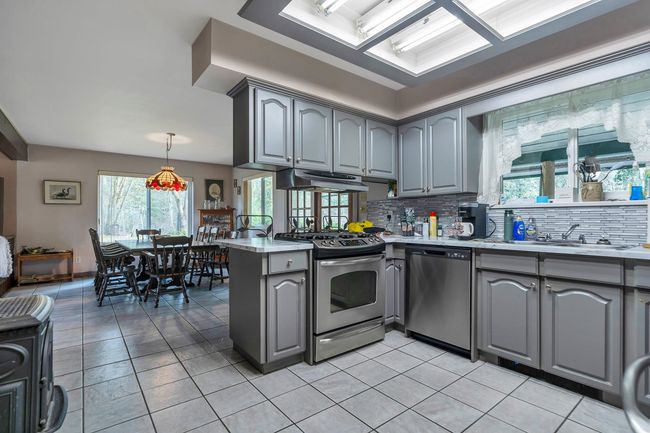 Kitchen with under cabinet range hood, gray cabinets, a peninsula, stainless steel appliances, and a sink | Image 10