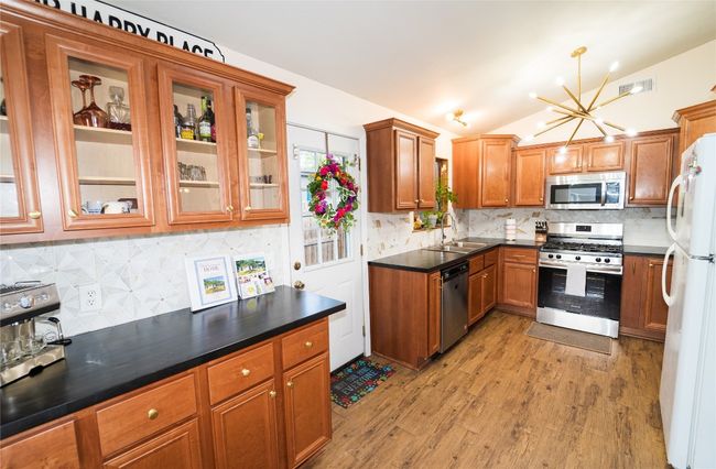 Kitchen featuring stainless steel appliances, tasteful backsplash, brown cabinetry, a chandelier, and vaulted ceiling | Image 11