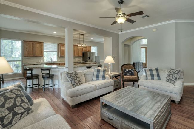 Living room with arched walkways, visible vents, ceiling fan, dark wood-type flooring, and ornamental molding | Image 9