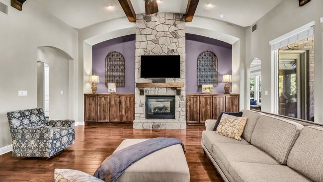 Living room featuring a stone fireplace, beamed ceiling, wood finished floors, arched walkways, and a high ceiling | Image 13