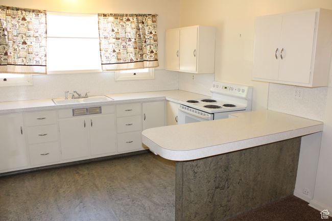Kitchen with white range with electric stovetop, light countertops, white cabinets, and a peninsula | Image 27