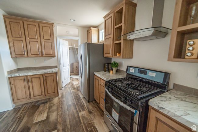 Kitchen featuring wall chimney range hood, open shelves, brown cabinetry, stainless steel appliances, and dark wood-type flooring | Image 47