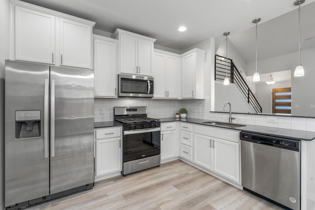 Kitchen with appliances with stainless steel finishes, a sink, dark countertops, decorative backsplash, and white cabinetry | Image 9