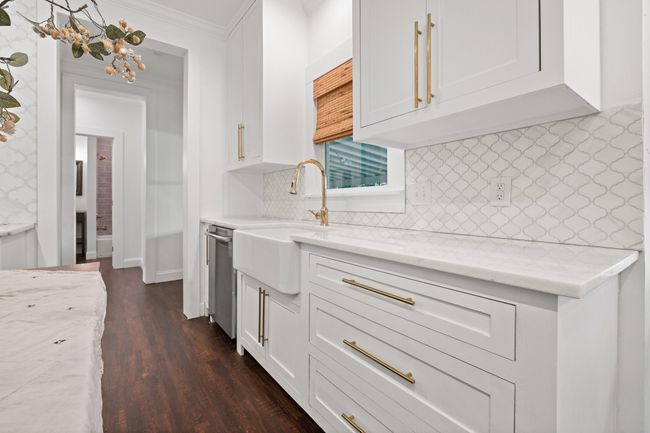 Kitchen featuring light stone countertops, white cabinets, stainless steel dishwasher, dark wood finished floors, and crown molding | Image 13