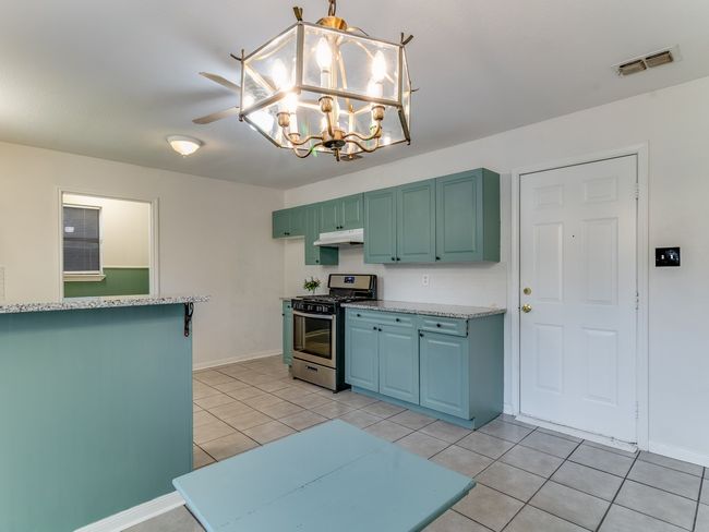 Kitchen with gas range, light tile patterned flooring, under cabinet range hood, a chandelier, and decorative light fixtures | Image 9