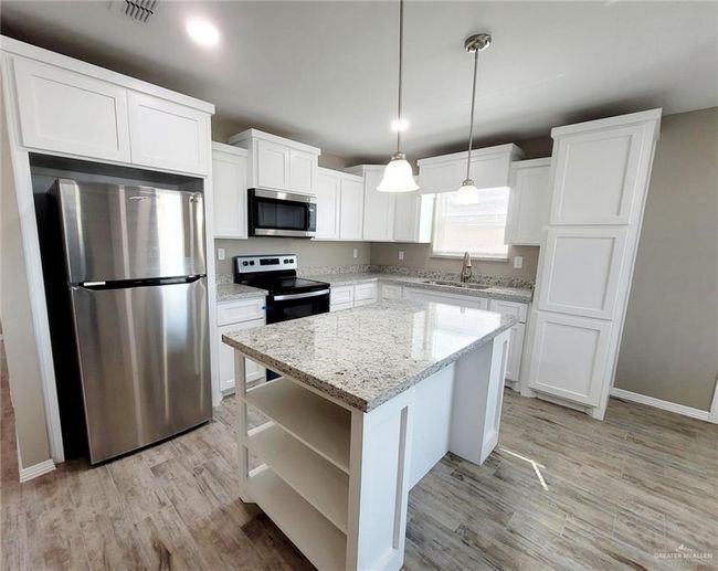 Kitchen with stainless steel appliances, open shelves, white cabinets, light wood-style floors, and a center island | Image 7