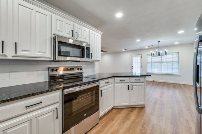 Kitchen with an inviting chandelier, appliances with stainless steel finishes, white cabinetry, light wood-style flooring, and decorative backsplash | Image 13