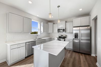 The kitchen features upgraded cabinetry, quartz countertops and picket style tile backsplash, beautifully accented by stainless appliances. The center island provides additional seating & prep space. | Image 2