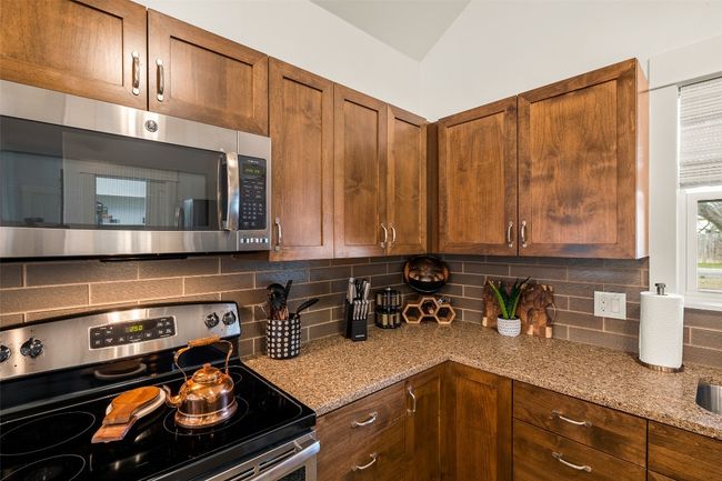 Kitchen with appliances with stainless steel finishes, backsplash, light stone counters, and brown cabinetry | Image 32