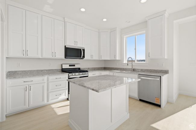 Kitchen featuring appliances with stainless steel finishes, white cabinetry, light stone countertops, light wood-style flooring, and recessed lighting | Image 7