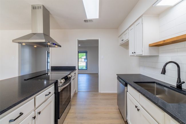 Kitchen featuring a sink, island range hood, white cabinetry, light wood-style flooring, and appliances with stainless steel finishes | Image 5