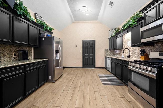 This kitchen features modern stainless-steel appliances, dark cabinetry, granite countertops, and a herringbone-patterned tile floor. It has a neutral color palette and is well-lit with a combination of natural and ceiling lighting. This is the Information center's kitchen located on the property | Image 30