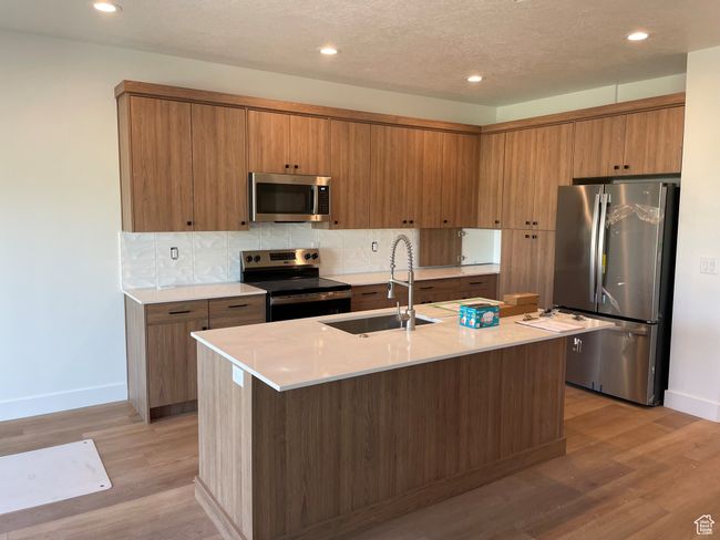 Kitchen featuring stainless steel appliances, recessed lighting, light countertops, brown cabinetry, and light wood-type flooring | Image 6
