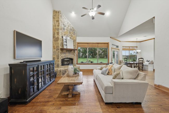 Living area with a ceiling fan, wood finished floors, high vaulted ceiling, a fireplace, and a chandelier | Image 9