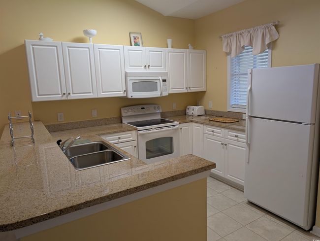 Kitchen featuring white cabinets, white appliances, a sink, light stone counters, and light tile patterned floors | Image 7