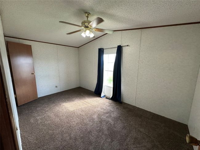 Carpeted empty room with a textured ceiling, a ceiling fan, and vaulted ceiling | Image 30