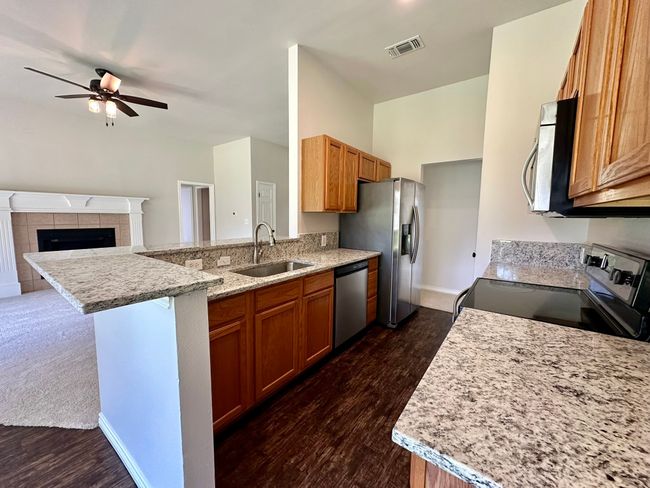 Kitchen featuring appliances with stainless steel finishes, dark wood-style flooring, a peninsula, a ceiling fan, and brown cabinetry | Image 5