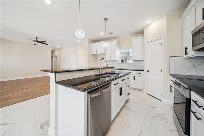 Kitchen with appliances with stainless steel finishes, a kitchen island with sink, sink, white cabinetry, and hanging light fixtures | Image 10