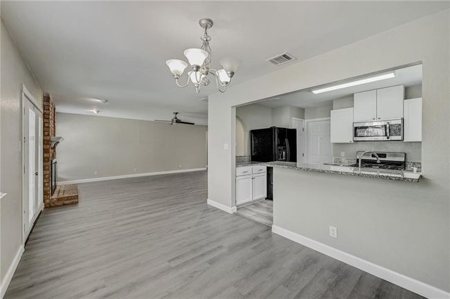 Kitchen with appliances with stainless steel finishes, a chandelier, ceiling fan, white cabinets, and light wood-style flooring | Image 6
