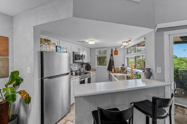 Kitchen featuring appliances with stainless steel finishes, a sink, white cabinetry, light countertops, and a breakfast bar | Image 6